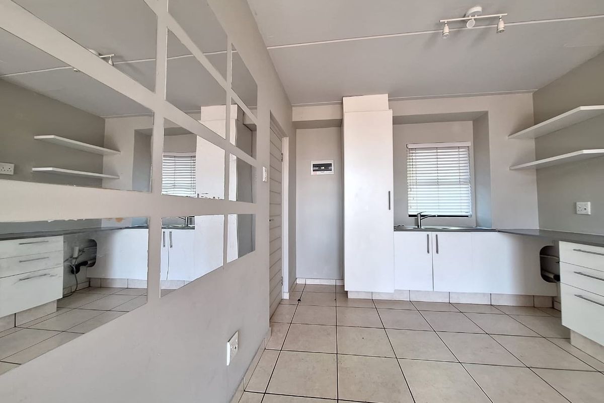 A compact, empty kitchen featuring white cabinetry, tiled flooring, and a stainless steel sink, offering a blank canvas for potential renovation or modernization.