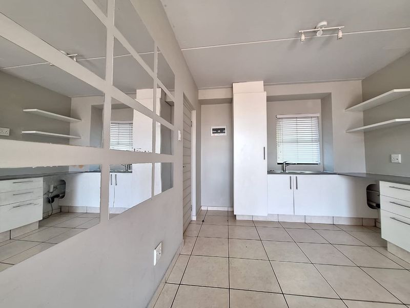 A compact, empty kitchen featuring white cabinetry, tiled flooring, and a stainless steel sink, offering a blank canvas for potential renovation or modernization.