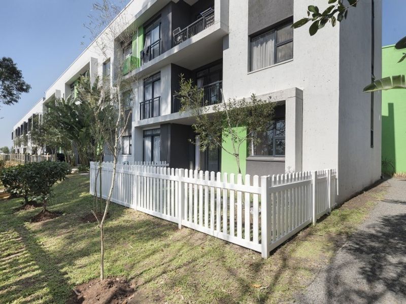 Exterior view of a modern apartment building featuring ground floor units with private fenced gardens and upper-level balconies.