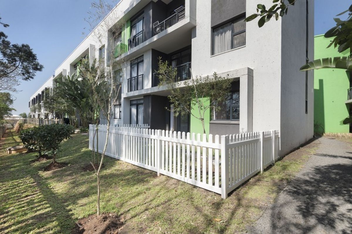 Exterior view of a modern apartment building featuring ground floor units with private fenced gardens and upper-level balconies.