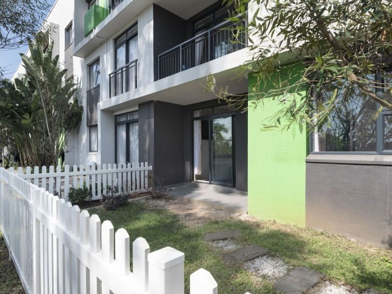 Ground floor apartment exterior featuring a private garden, white picket fence, concrete patio, and sliding door access to the living area.