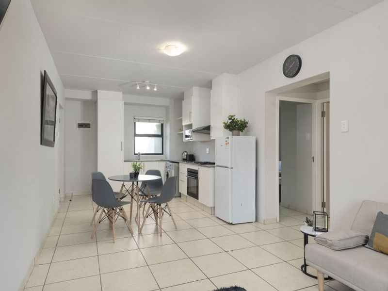 Open-plan living and kitchen area featuring tiled flooring, functional cabinetry, and integrated kitchen appliances in a bright, neutral space.