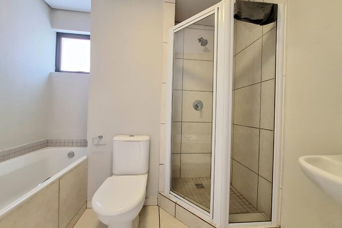 A functional bathroom featuring a built-in bathtub, a separate corner shower enclosure, a toilet, and a wall-mounted basin with neutral tiling.