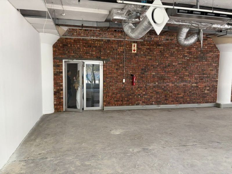 An open-plan office space featuring industrial-style exposed brick walls, concrete flooring, and exposed HVAC ducting, providing a blank canvas for custom fit-out.