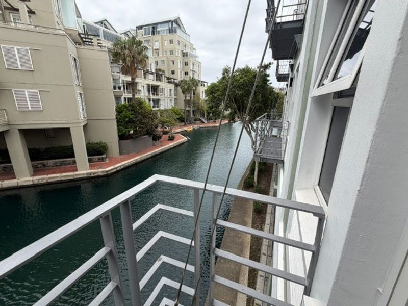 A view from a balcony overlooking a canal and surrounding residential buildings, featuring a metal safety railing and external fire escape access.