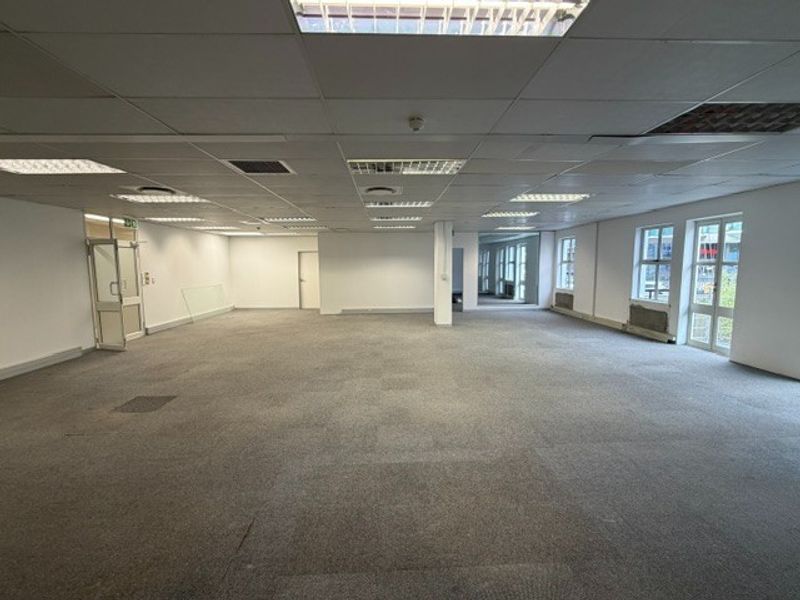 A large, open-plan office space featuring a suspended ceiling, recessed lighting, and expansive windows, providing a blank canvas for professional workspace customization.