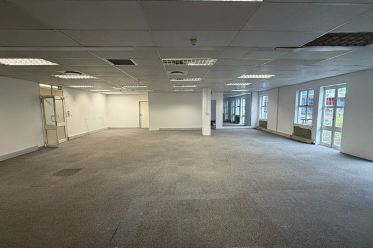 A large, open-plan office space featuring a suspended ceiling, recessed lighting, and expansive windows, providing a blank canvas for professional workspace customization.