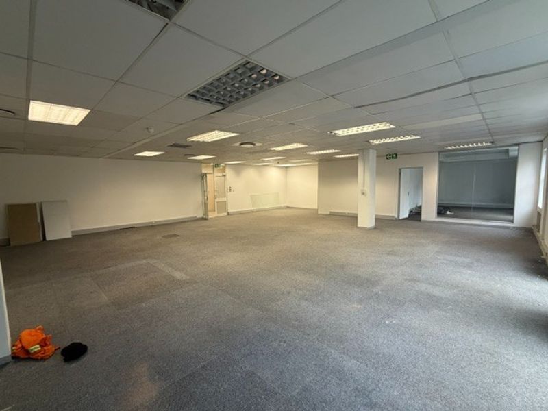 A spacious, open-plan office area featuring a suspended ceiling with recessed lighting, carpeted flooring, and a glass partition, ready for custom fit-out.