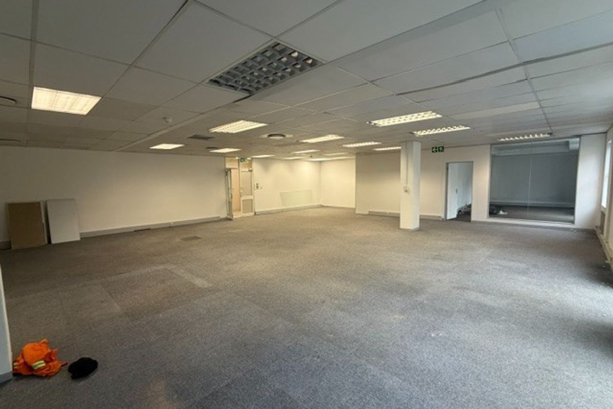 A spacious, open-plan office area featuring a suspended ceiling with recessed lighting, carpeted flooring, and a glass partition, ready for custom fit-out.
