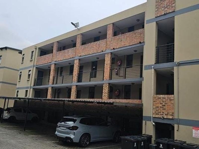 Exterior view of a multi-story apartment complex featuring brick accents, private balconies with metal railings, and a covered ground-level parking area.