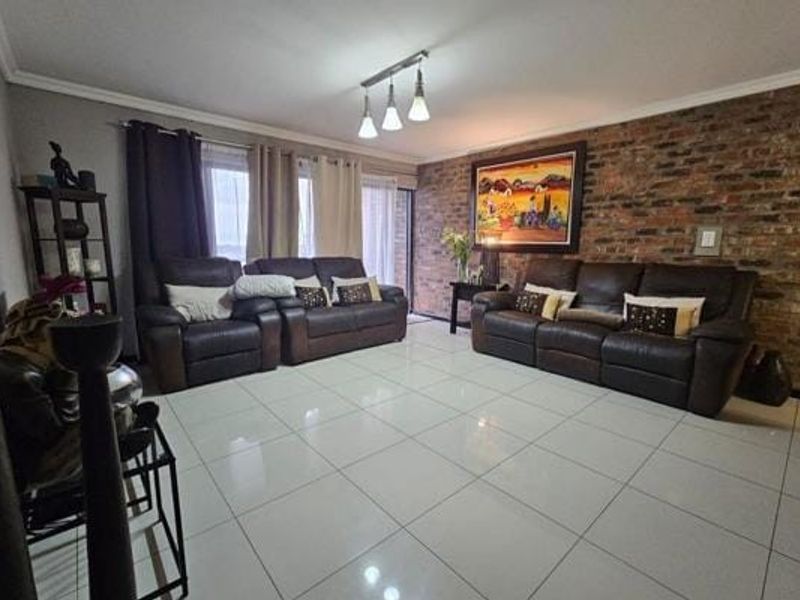 Spacious living room featuring a prominent exposed brick feature wall, polished tiled flooring, and direct access to an outdoor area via sliding glass doors.