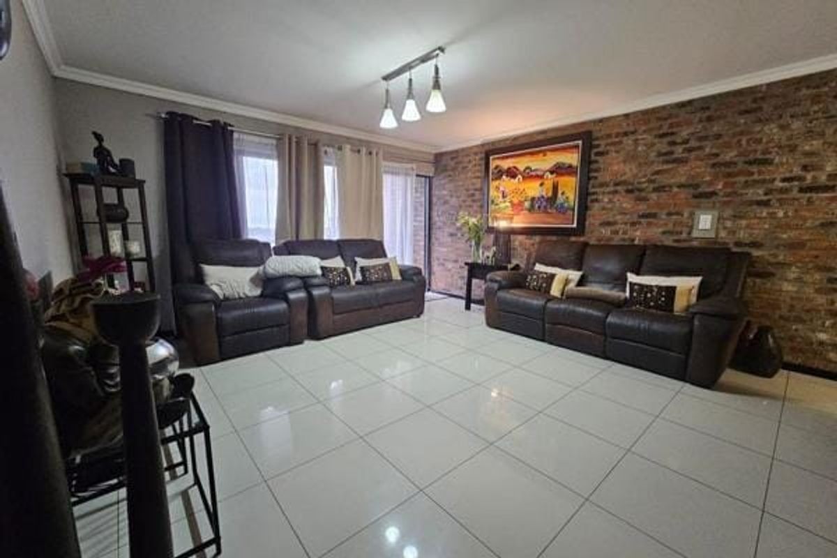 Spacious living room featuring a prominent exposed brick feature wall, polished tiled flooring, and direct access to an outdoor area via sliding glass doors.