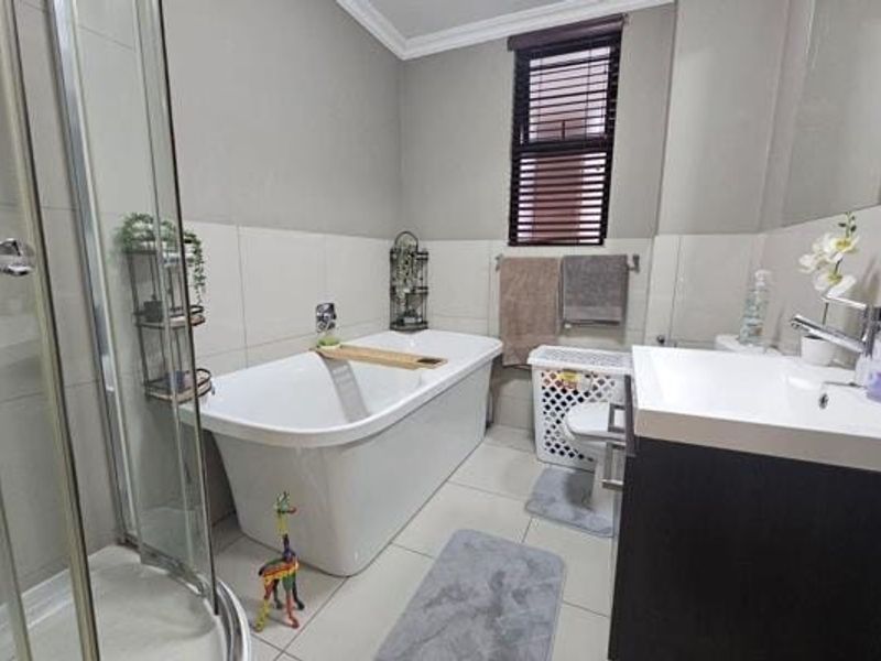 Modern bathroom featuring a freestanding bathtub, glass shower enclosure, vanity with basin, and neutral wall and floor tiling.
