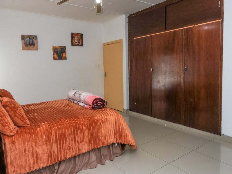 A bedroom featuring tiled flooring, a ceiling fan, and a large built-in wooden wardrobe providing ample storage space.