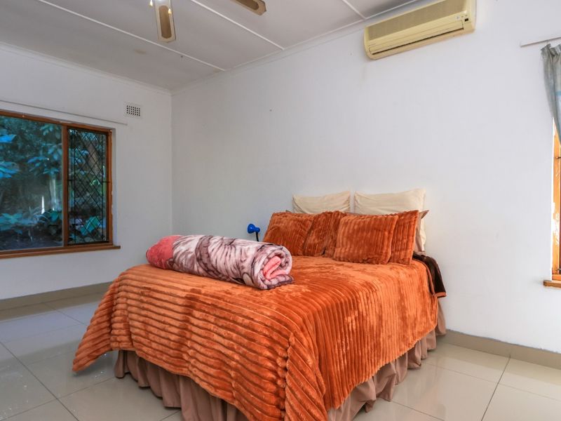 A bedroom featuring tiled flooring, a ceiling fan, and a wall-mounted split-system air conditioner, with windows fitted with security bars.