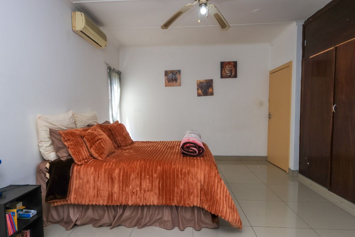 A bedroom featuring tiled flooring, built-in cupboards, a ceiling fan, and an air conditioning unit.