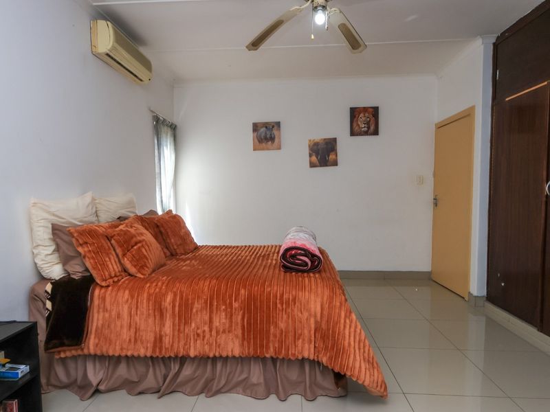 A bedroom featuring tiled flooring, built-in cupboards, a ceiling fan, and an air conditioning unit.
