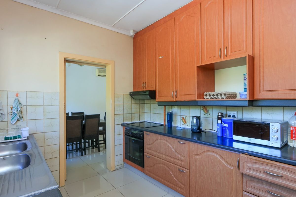 A functional kitchen featuring wood-look laminate cabinetry, a double stainless steel sink, built-in oven, and electric hob with tiled backsplash.