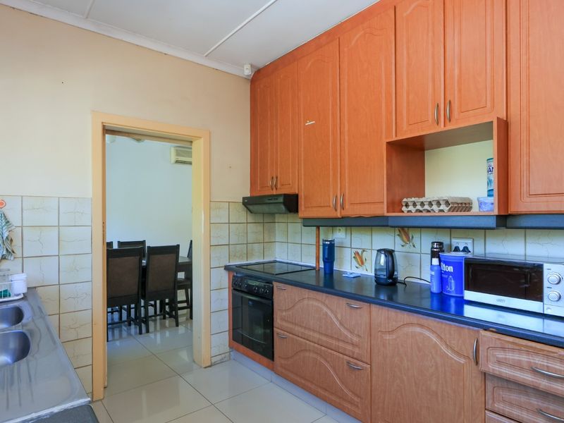 A functional kitchen featuring wood-look laminate cabinetry, a double stainless steel sink, built-in oven, and electric hob with tiled backsplash.