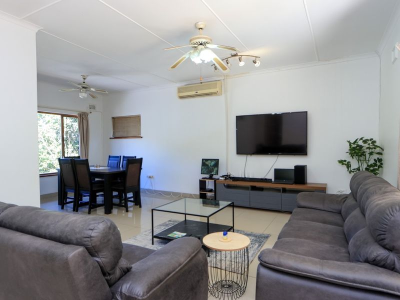 Spacious open-plan living and dining area featuring tiled flooring, ceiling fans, and a wall-mounted air conditioning unit.