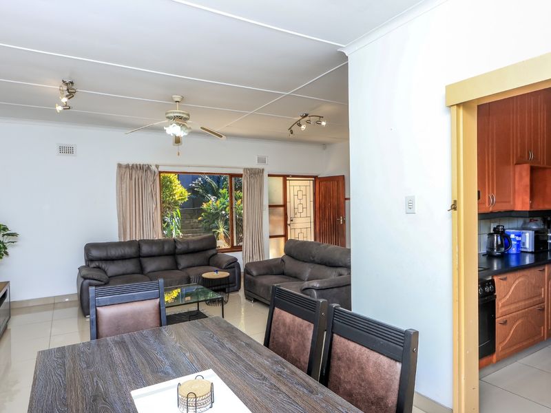 Open-plan living and dining area featuring tiled floors, ceiling fan, and an adjacent kitchen with built-in cabinetry and dark countertops.