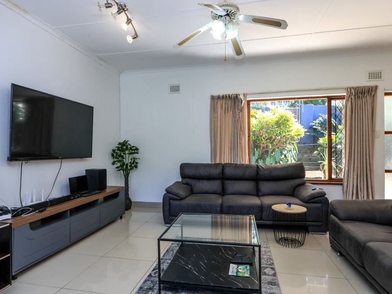 A spacious living room featuring tiled flooring, a ceiling fan, track lighting, and an air conditioning unit, with direct access to the outdoor area.