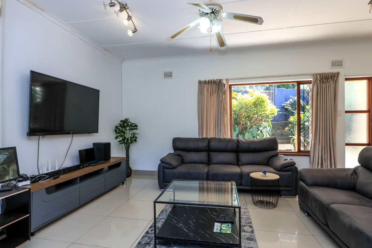 A spacious living room featuring tiled flooring, a ceiling fan, track lighting, and an air conditioning unit, with direct access to the outdoor area.