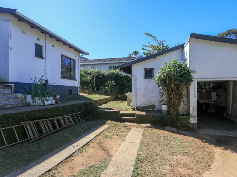 Rear exterior view showing a detached garage, concrete driveway, and tiled steps leading to the main house structure.