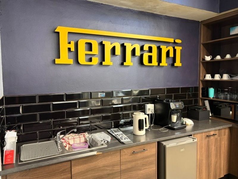 A compact kitchenette area featuring dark subway tile backsplash, wood-finish cabinetry, stainless steel sink, and open shelving for storage.