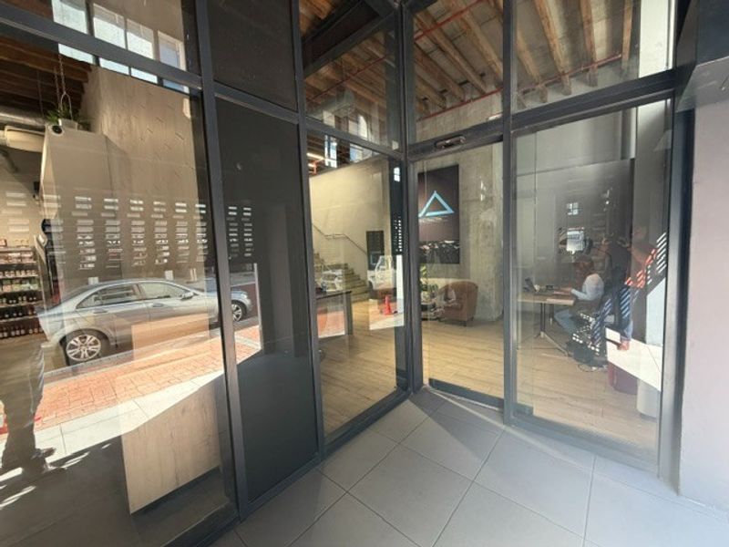 Modern retail entrance featuring a glass storefront facade, exposed timber ceiling beams, and tiled flooring, providing a bright and professional street-level access point.