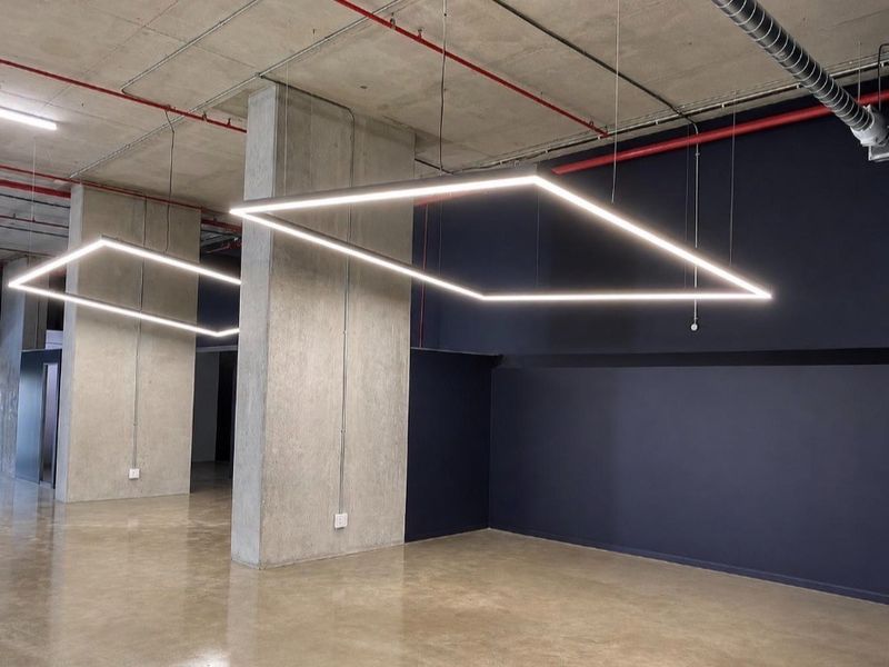 Modern open-plan retail or office space featuring polished concrete floors, exposed industrial ceilings, and contemporary suspended square LED lighting fixtures.