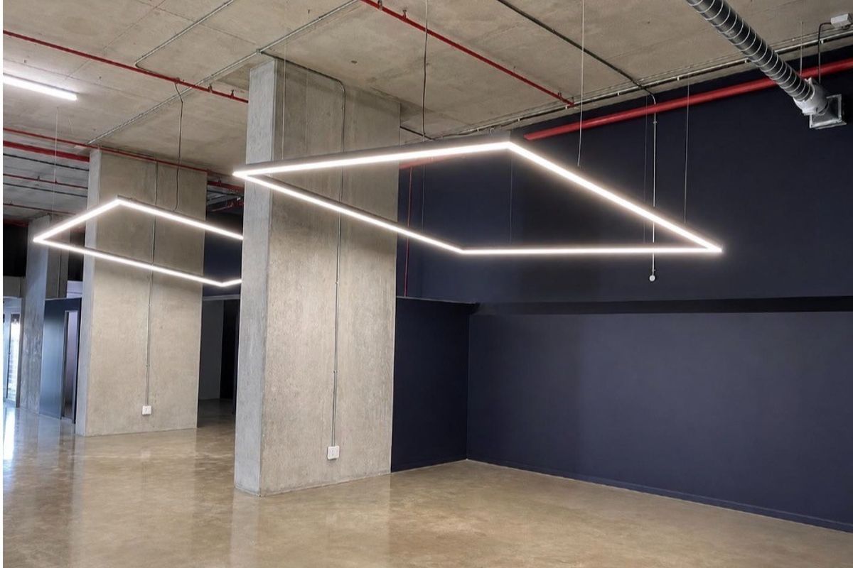 Modern open-plan retail or office space featuring polished concrete floors, exposed industrial ceilings, and contemporary suspended square LED lighting fixtures.