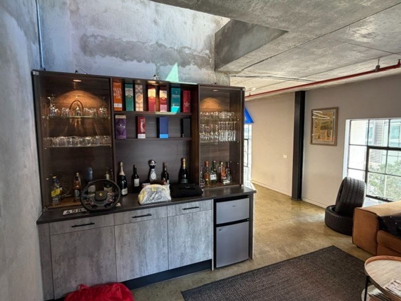 Industrial-style bar area featuring custom built-in cabinetry, integrated lighting, polished concrete floors, and exposed structural elements in an open-plan retail or studio space.
