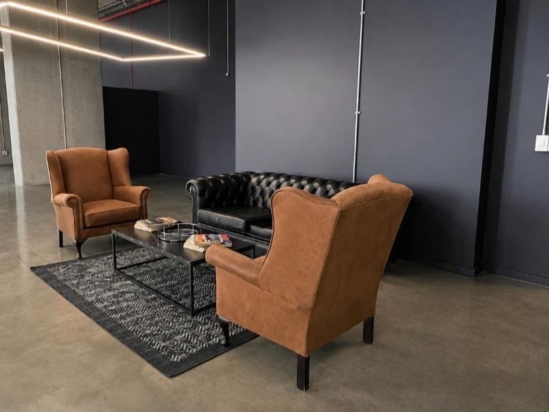 Modern industrial-style lounge area featuring polished concrete floors, exposed conduit, and contemporary suspended linear lighting in a spacious open-plan setting.