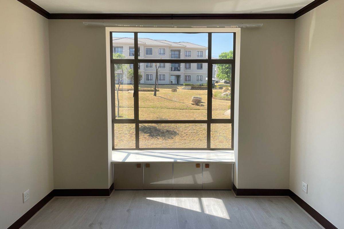 A bright, empty bedroom featuring light laminate flooring, dark trim accents, and a large window with integrated built-in storage cabinetry.