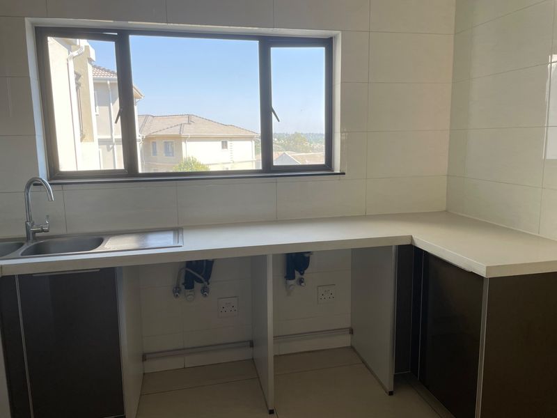 A clean, modern kitchen area featuring stone countertops, a stainless steel sink, and tiled finishes, ready for appliance installation.