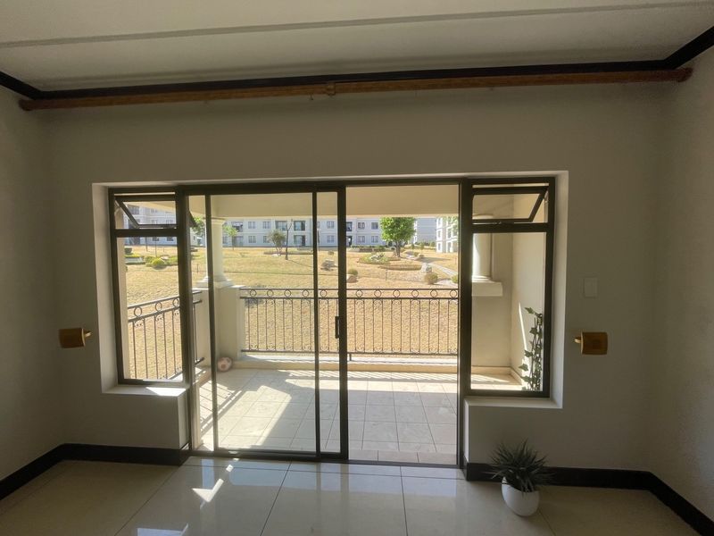 A bright, empty living area featuring tiled floors and large sliding glass doors that open onto a private balcony with garden views.