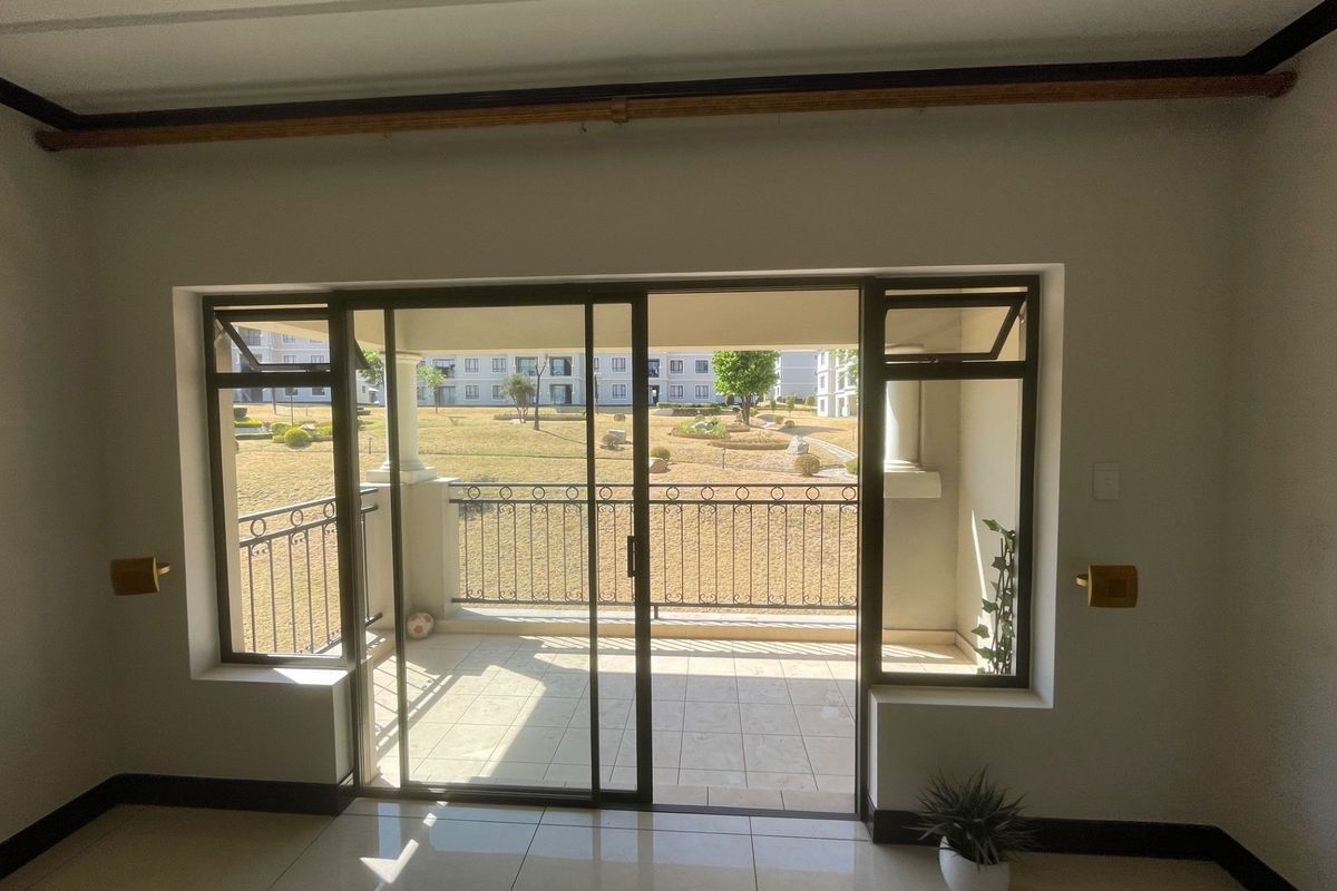A bright, empty living area featuring tiled floors and large sliding glass doors that open onto a private balcony with garden views.