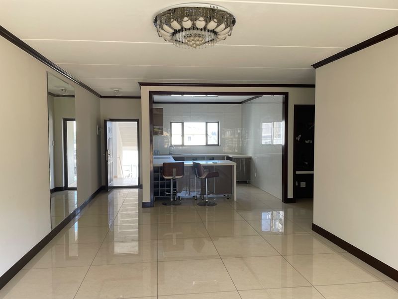 Open plan living area featuring polished tiled floors, a modern kitchen with island, and a decorative ceiling light fixture.