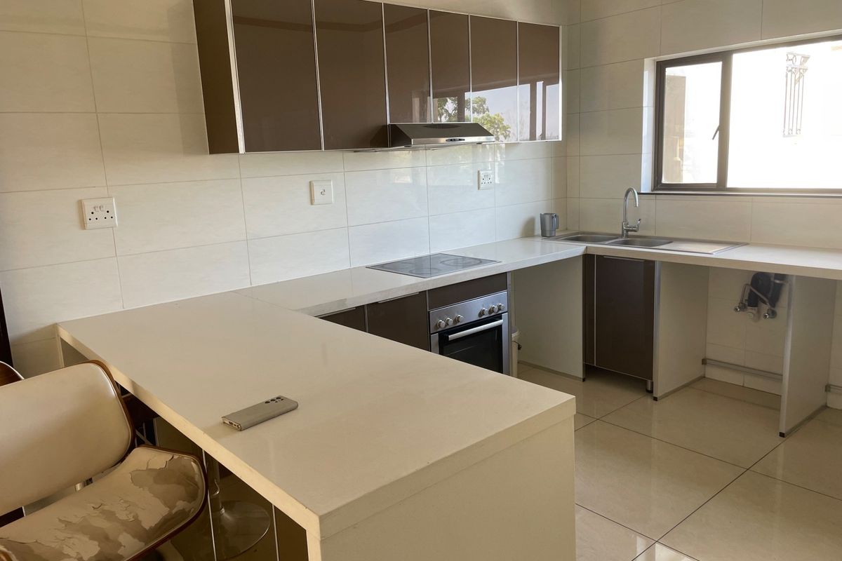 Modern kitchen featuring sleek brown cabinetry, stone countertops, integrated electric hob and oven, and tiled finishes throughout.