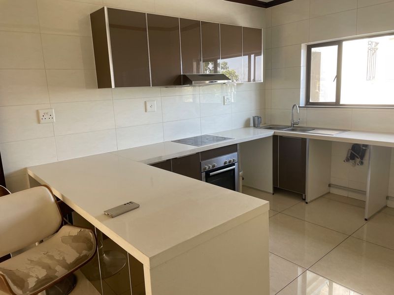 Modern kitchen featuring sleek brown cabinetry, stone countertops, integrated electric hob and oven, and tiled finishes throughout.