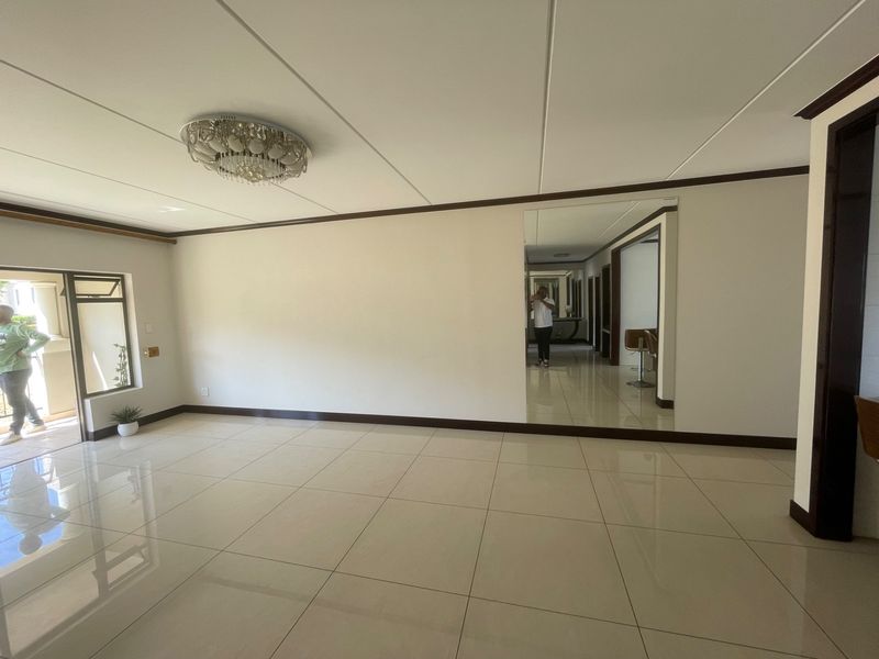 A spacious, empty living area featuring polished tiled flooring, a large wall mirror, and a ceiling-mounted light fixture, leading to an outdoor patio area.