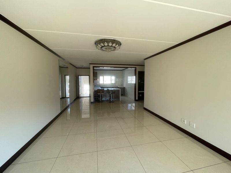 Spacious open-plan living area featuring polished tile flooring, a mirrored wall, and a view through to the modern kitchen area.