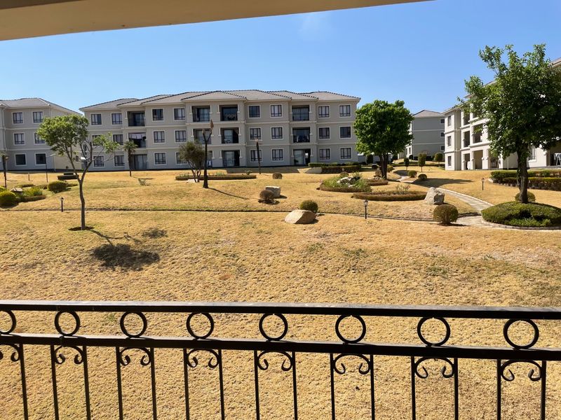 A view from a balcony overlooking a well-maintained communal garden area and surrounding apartment buildings within the residential complex.