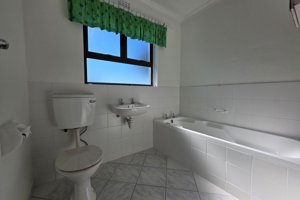 A functional bathroom featuring a built-in bathtub, wall-mounted basin, and toilet with white tiled finishes and neutral floor tiles.