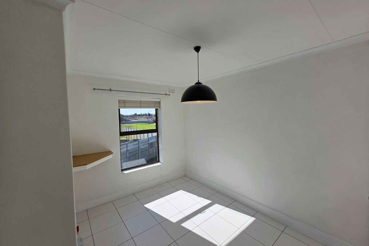 A bright, empty bedroom featuring white tiled flooring, a built-in corner shelf, and a modern pendant light fixture.