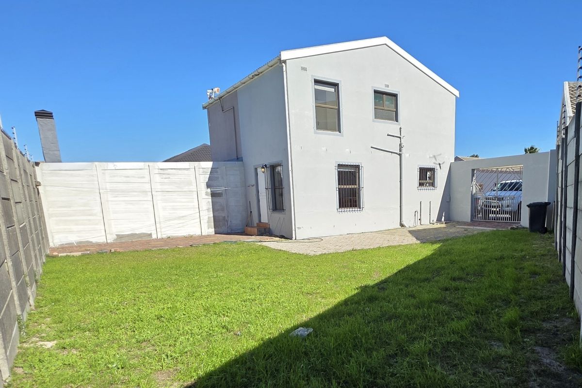 Rear view of the townhouse featuring a private garden, paved patio area, and secure boundary walls with gated access.