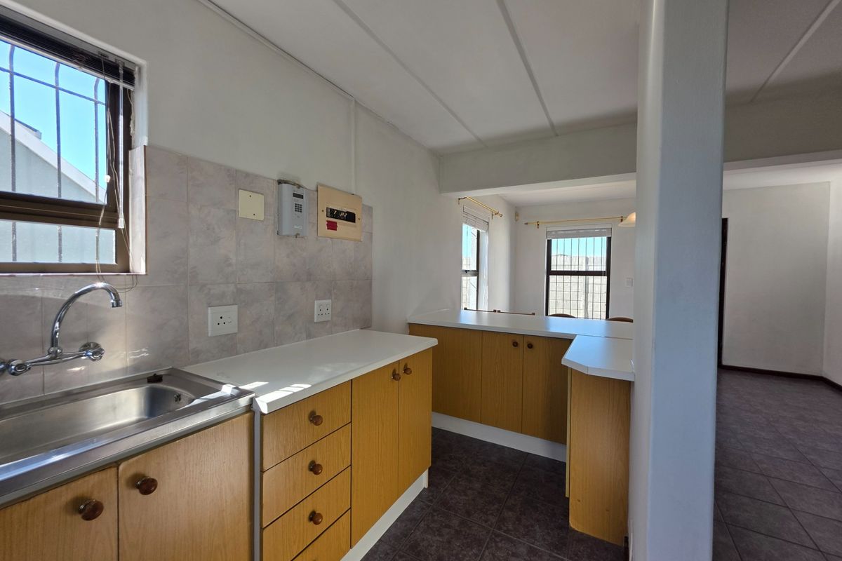 A functional kitchen featuring laminate cabinetry, tiled backsplash, and a stainless steel sink, with an open-plan layout connecting to the adjacent living area.