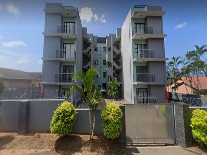 Front elevation of a multi-story apartment complex featuring modern grey facade, private balconies, secure perimeter wall with electric fencing, and gated access.