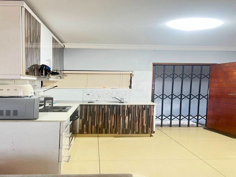 A functional kitchen featuring modern cabinetry, stone countertops, tiled flooring, and direct access to an exterior area through a secure gate and wooden door.